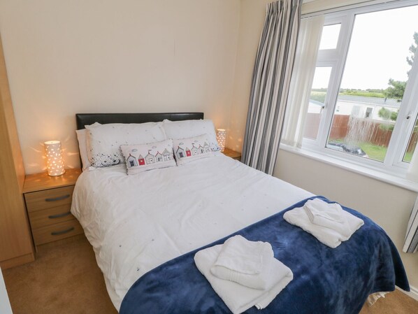 A neatly made bed with white bedding and blue accents, a bedside table with a lamp, and a window with curtains.