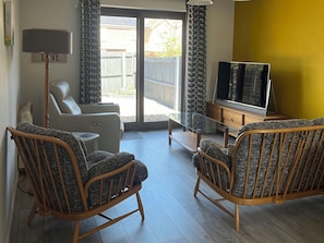 Ett vardagsrum med två fåtöljer i rotting, en soffa, en tv och en lampa.