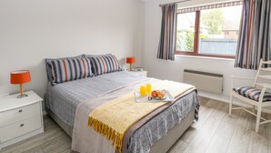 A bedroom with a bed, bedside tables, a lamp, a window with curtains, and a chair. - Village Retreat (Ely)