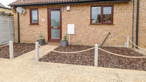 A brick building with a tiled roof, a front door, and two windows. There is a satellite dish on the left and a sign on the right. - Village Retreat (Ely)