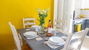 A dining table set with plates, cutlery, a vase with flowers, and a bottle, against a yellow wall. - Village Retreat (Ely)