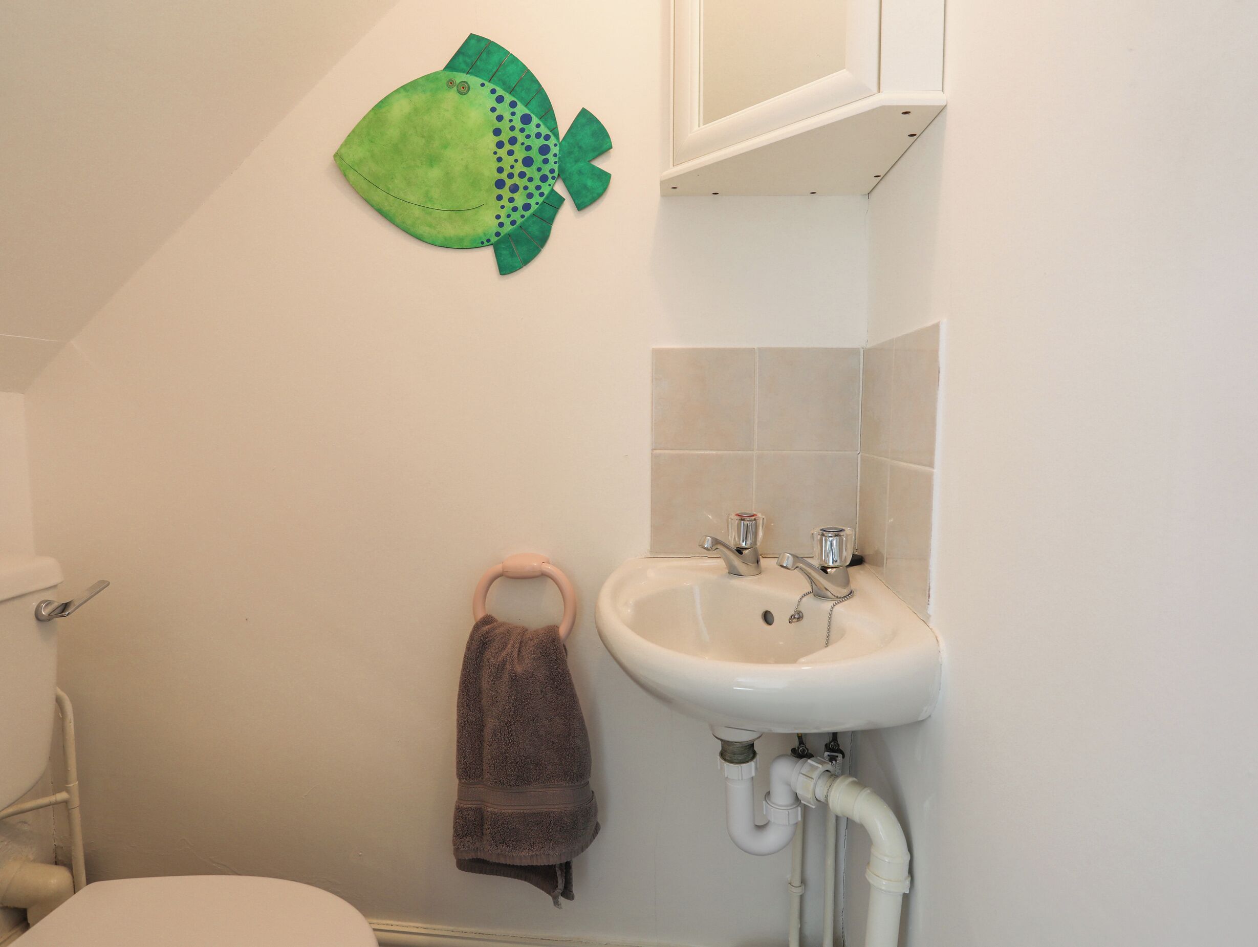 A bathroom with a white sink, a towel rack, and a green fish decoration on the wall.