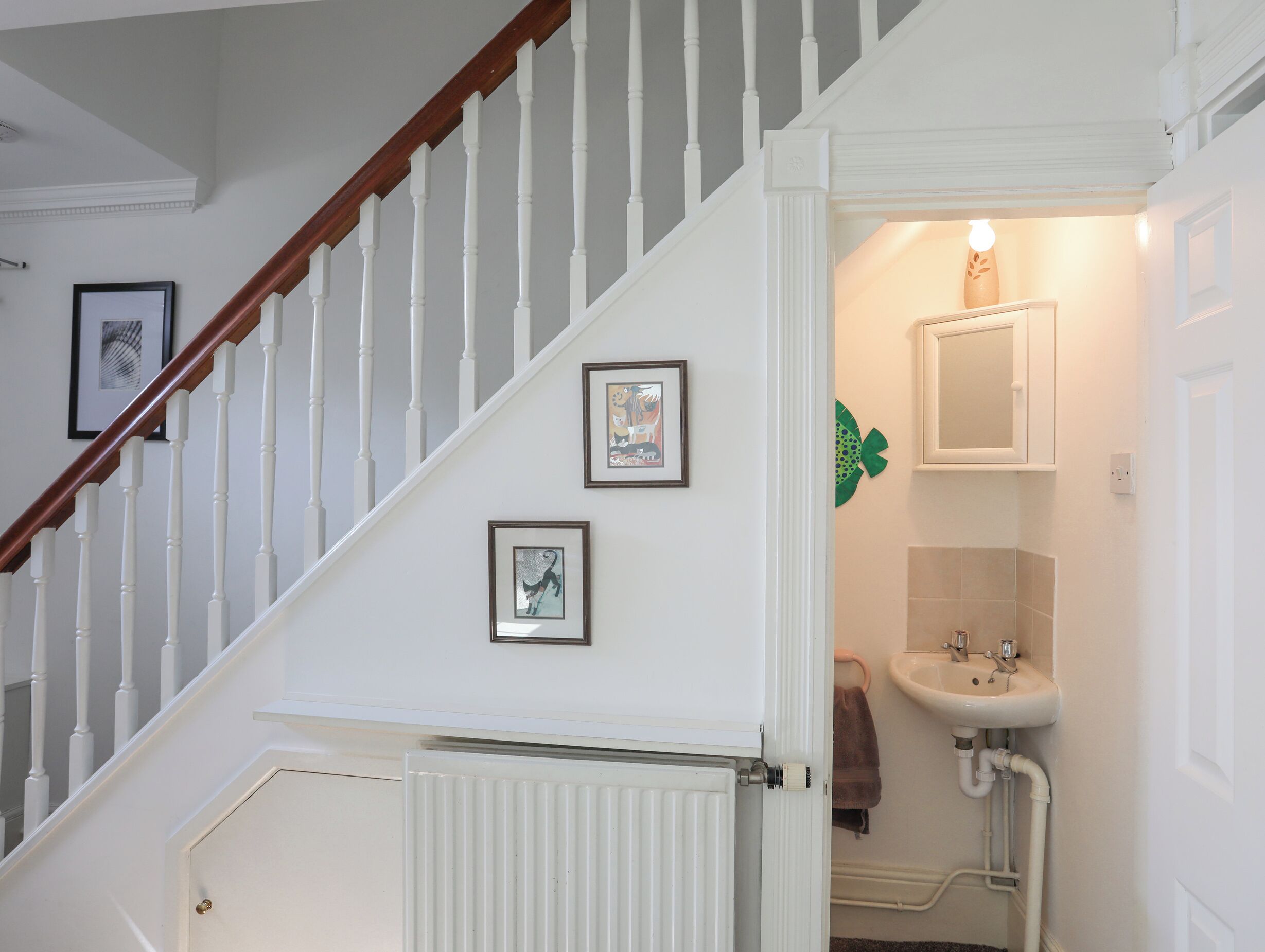 Un escalier avec des rampes blanches et une main courante en bois, menant à une salle de bain dotée d’un lavabo blanc et d’une serviette accrochée au mur.