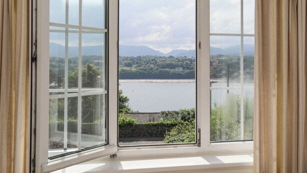 Ein Zimmer mit großem Erkerfenster mit Blick auf einen See, Berge und eine Stadt in der Ferne.