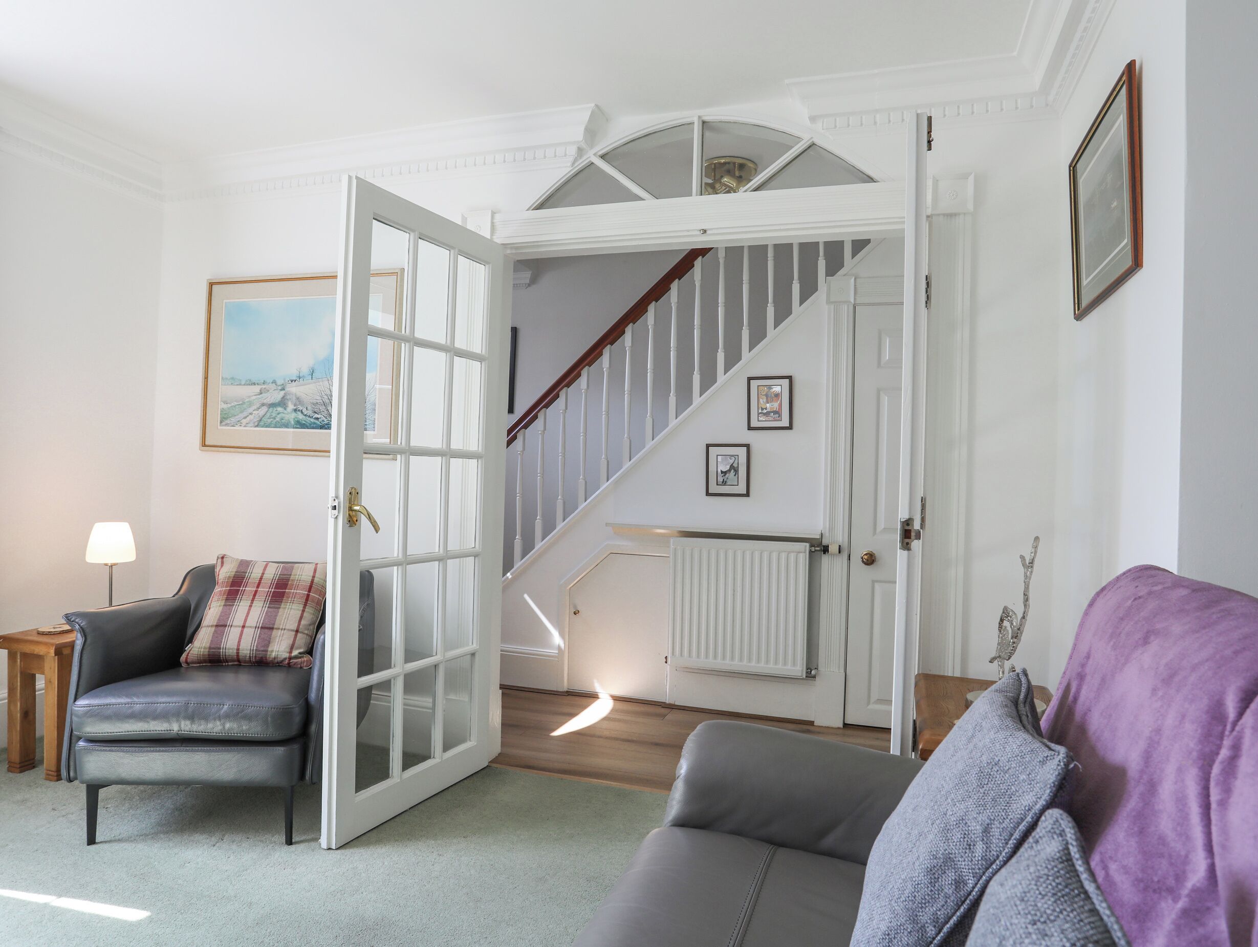 A living room with a sofa, a chair, a lamp, and a staircase leading to an upper floor.