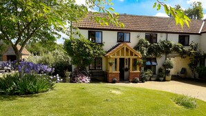 A two-story house with a small porch, surrounded by a well-maintained garden with various plants and flowers. - Berrys Place Farm Cottage (Gloucester)