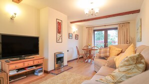 A cozy living room with a flat-screen TV, wooden entertainment unit, fireplace, and a comfortable sofa. - Berrys Place Farm Cottage (Gloucester)