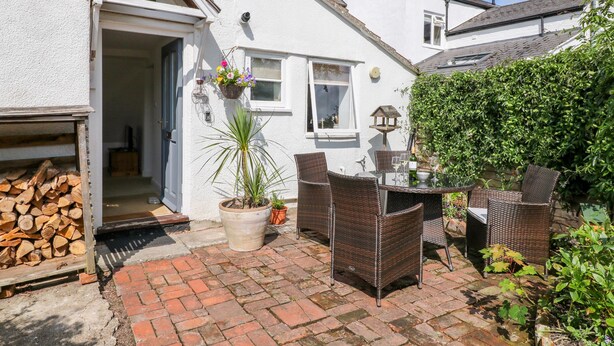Une maison blanche avec un patio en briques, des meubles en osier et une plante en pot.