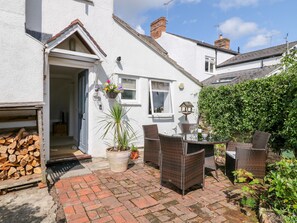 A white house with a brick patio, wicker furniture, and a potted plant. - Boo Cottage (Taunton)