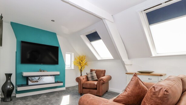 Un salon moderne avec un mur d’accent de couleur turquoise, un téléviseur à écran plat, une cheminée, un canapé en cuir marron et une lucarne.