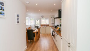A modern kitchen with wooden flooring, white cabinetry, and a dining area with a table set for four. - Llwyd Coed Canol (Caernarfon)