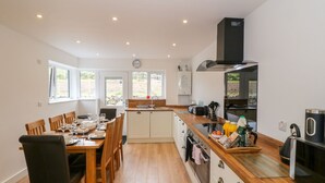 A modern kitchen with wooden flooring, white cabinets, and a central island with various appliances and items. - Llwyd Coed Canol (Caernarfon)