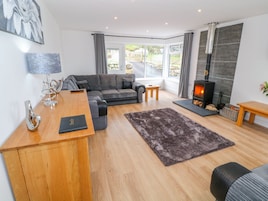 A modern living room with a sofa, a wooden desk, a fireplace, and a view through large windows.