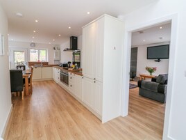 A modern kitchen with white cabinets, a dining area with a wooden table and chairs, and a living room with a sofa and a flat-screen TV.