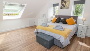 A modern bedroom with a sloped ceiling, a bed with multiple pillows, a bench, and a bedside table with a lamp. - Llwyd Coed Canol (Caernarfon)