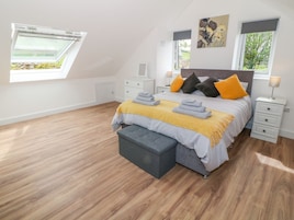 A modern bedroom with a sloped ceiling, a bed with multiple pillows, a bench, and a bedside table with a lamp.