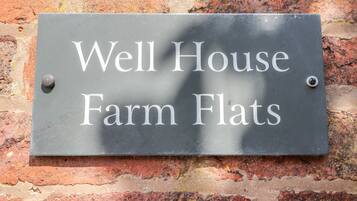 A sign with the text "Well House Farm Flats" mounted on a brick wall.