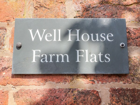 A sign with the text "Well House Farm Flats" mounted on a brick wall.