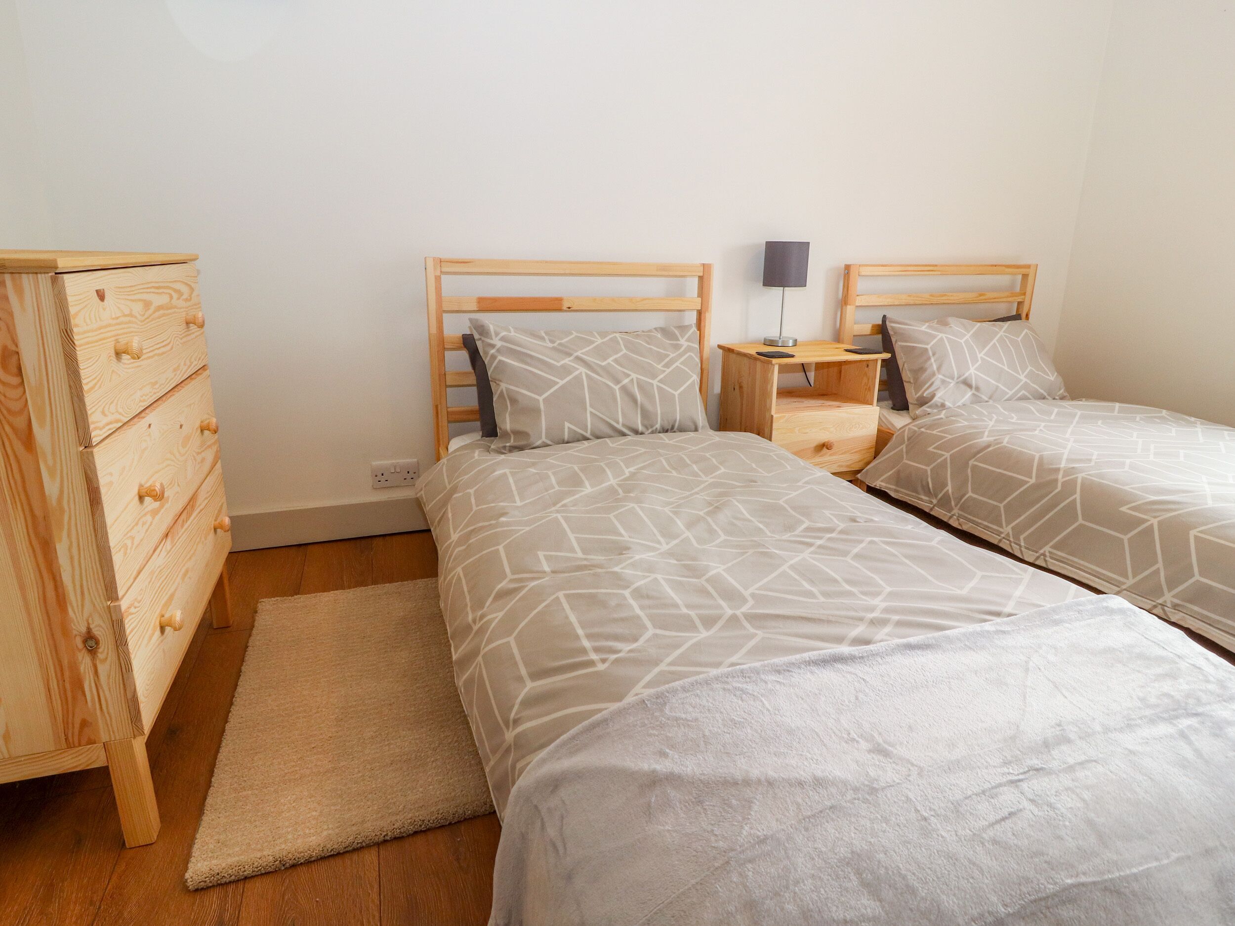 Une chambre avec deux lits, une commode en bois, une table de chevet et une lampe.