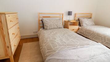 Une chambre avec deux lits, une commode en bois, une table de chevet et une lampe.