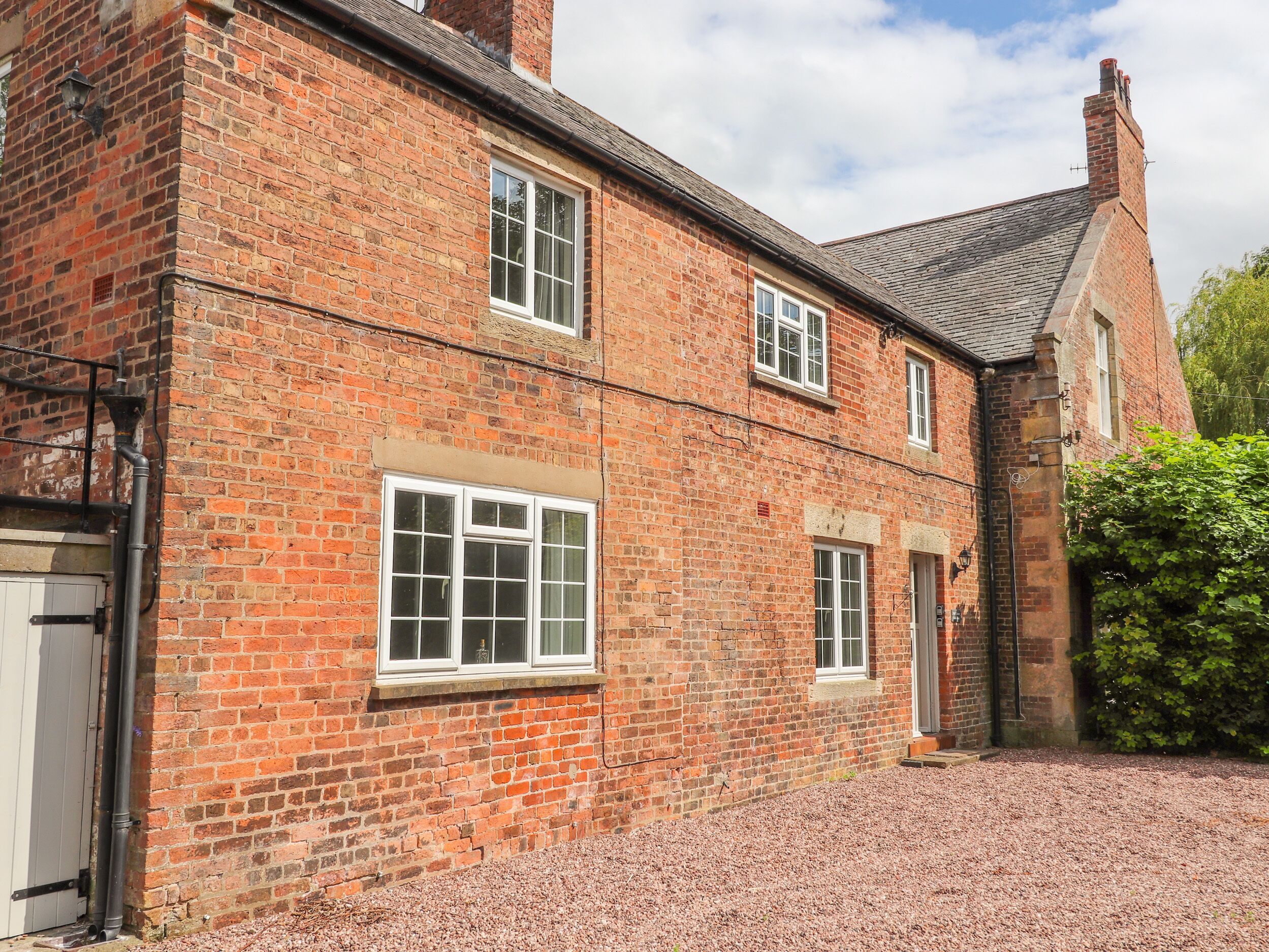 A traditional brick building with multiple windows and a gravel driveway.