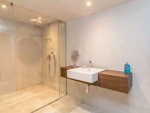 Une salle de bain moderne avec une douche à parois de verre, un lavabo blanc et un meuble-lavabo en bois, ainsi qu’un miroir.