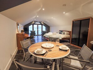 Une pièce compacte et bien éclairée, avec une table à manger dressée pour quatre personnes, un lit offrant une belle vue et une grande porte coulissante.