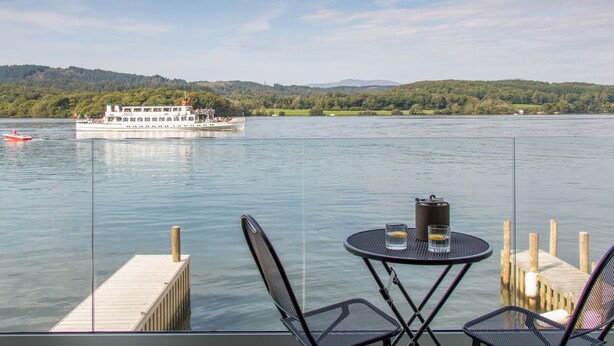 A lakeside view with a boat, dock, and outdoor seating area. - The Boat House at Louper Weir (Windermere)