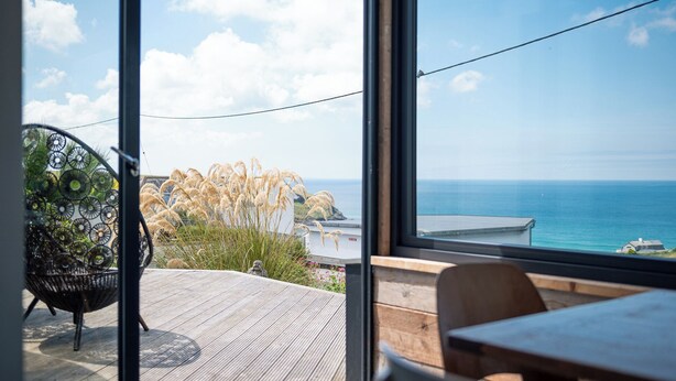 A modern room with a large glass window overlooking a coastal view. - Blue Bay Beach House (Newquay)