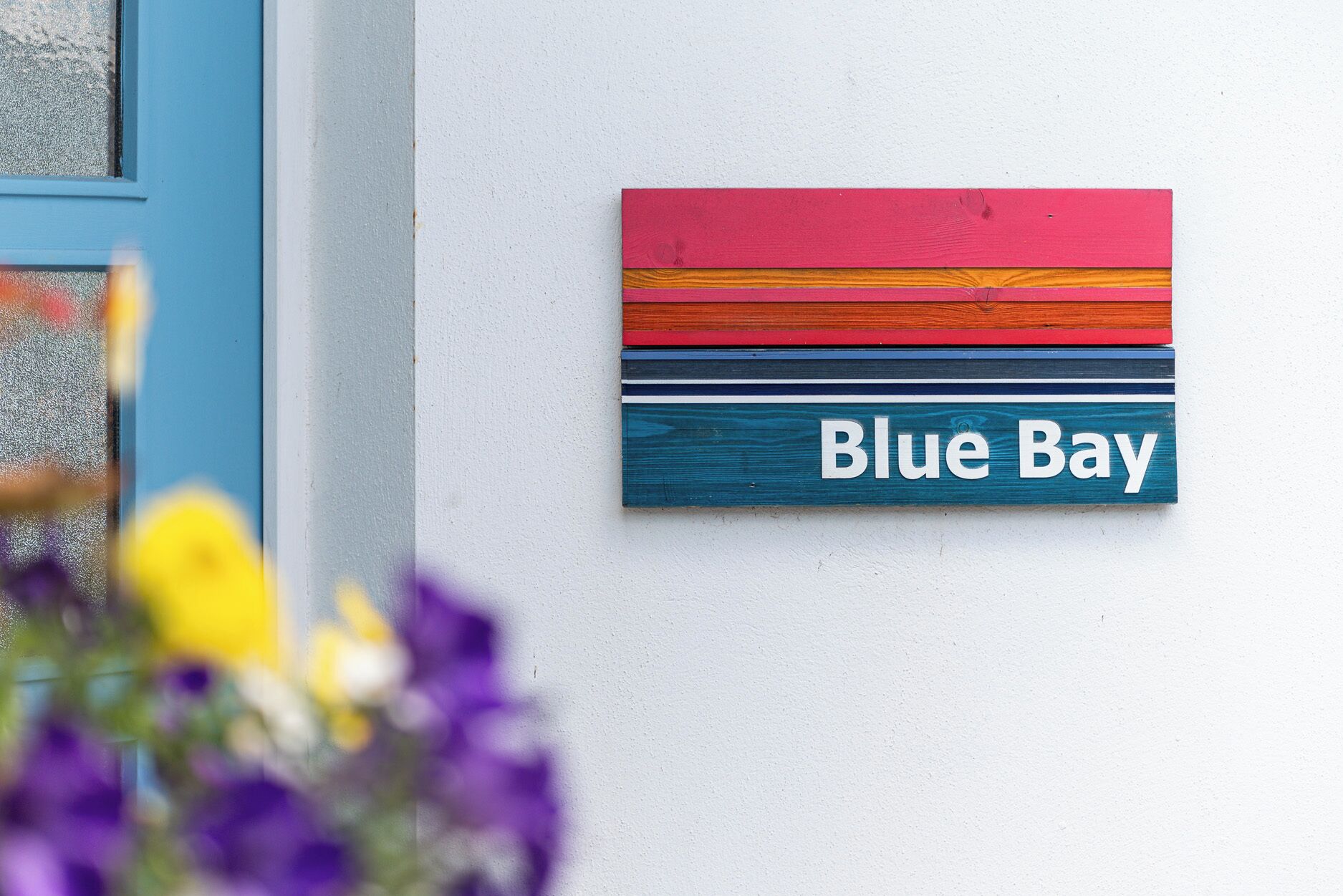 A colorful street sign with 'Blue Bay' written on it, mounted on a white wall.