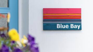 A colorful street sign with 'Blue Bay' written on it, mounted on a white wall.