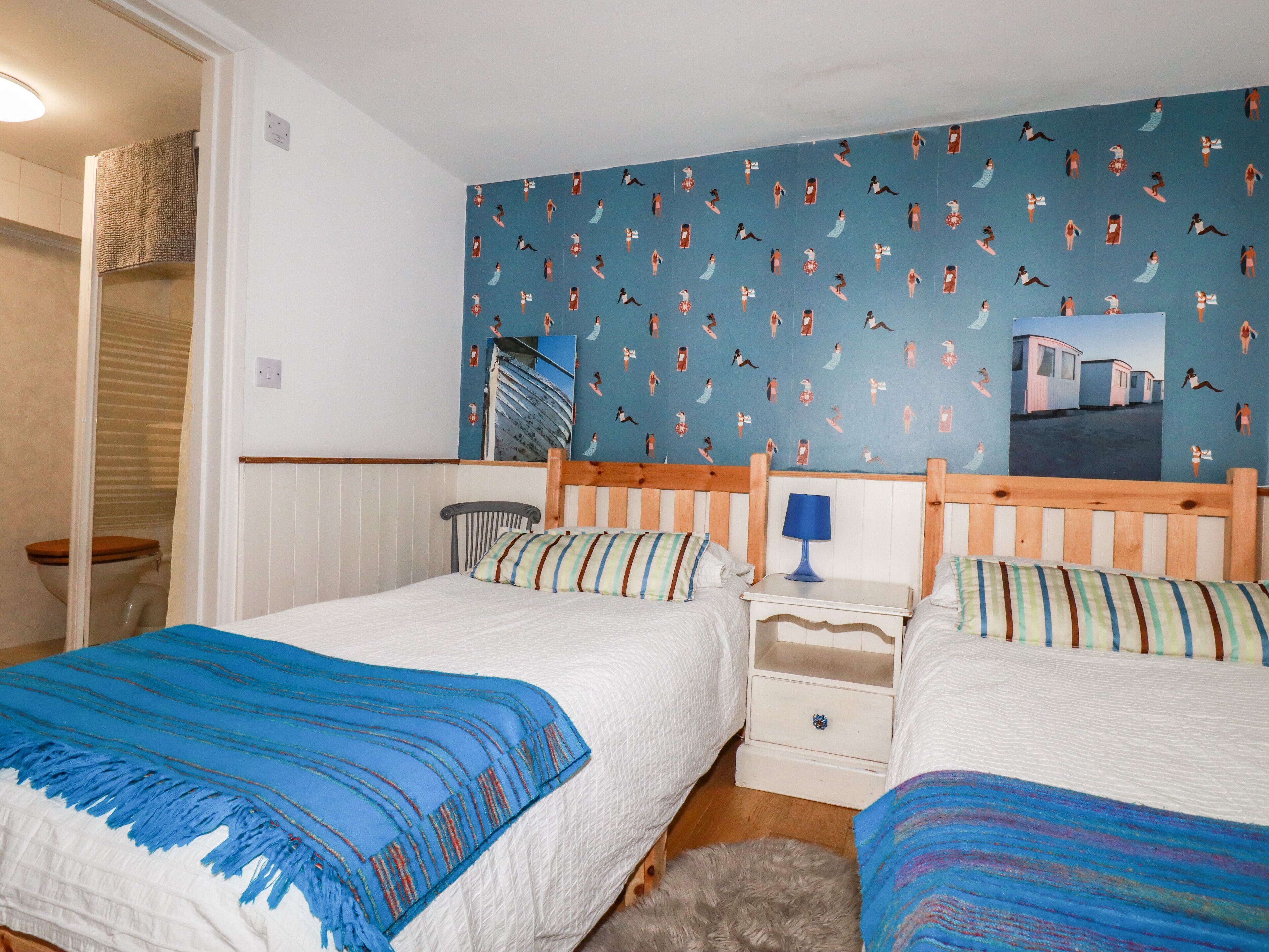 Un dormitorio con dos camas, una mesita de noche, una lámpara y un papel tapiz estampado.