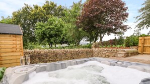 Un bain à remous doté d’un mur en pierre et d’une terrasse en bois, entouré d’arbres et d’une clôture en bois.