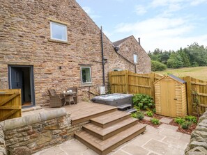 Une maison en pierre avec une terrasse en bois, un espace salon extérieur et un jacuzzi.