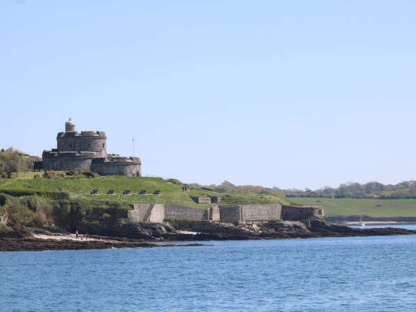 A coastal fortification with a prominent round tower, surrounded by grassy terrain and a body of water.