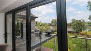 En modern balkong med en glasdörr, ett metallräcke och utsikt över en sjö och grönområden.