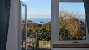 A room with a large window offering a view of the sea and hills. - Glenhaven (Tintagel)