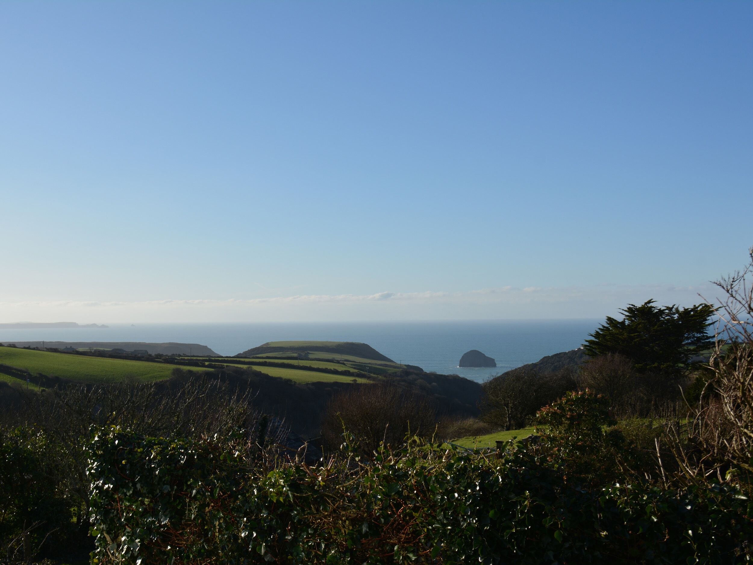 A coastal landscape with rolling hills and a distant view of the sea.