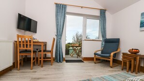 A cozy room with a wooden desk, a blue chair, a television, and a view through a glass door. - Glenhaven (Tintagel)