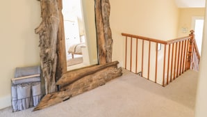 Een kamer met een grote spiegel, omlijst door een rustiek houten decorstuk, een trap met houten leuningen en een deur naar een andere kamer.