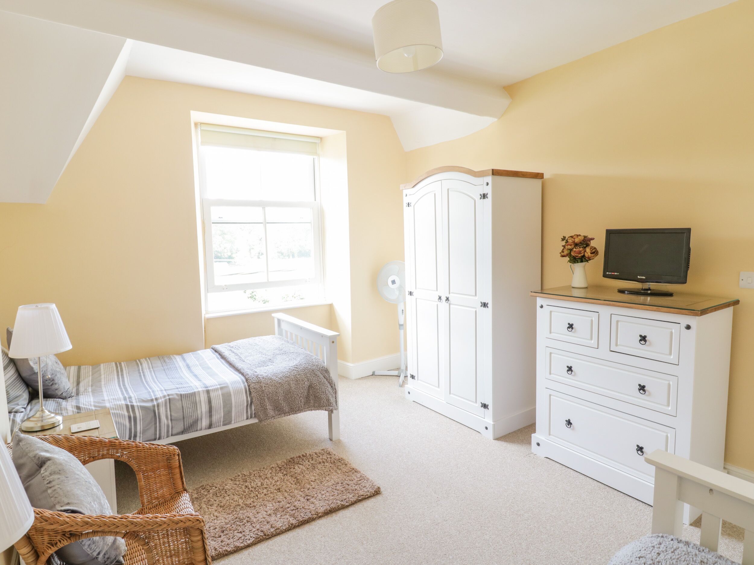 A bedroom with a bed, a dresser, a television, a lamp, and a window.