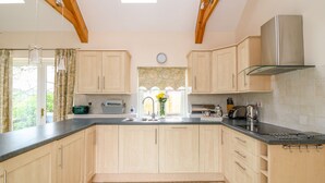 A kitchen with wooden cabinets, a black countertop, a stainless steel range hood, and a skylight. - Forget-me-not (St. Columb Major)