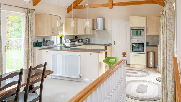A kitchen with wooden beams, a central island, and a dining area with a table and chairs. - Forget-me-not (St. Columb Major)