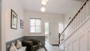 A hallway with a wooden staircase, a bench with cushions, a door leading outside, and a window with blinds. - Royal Victoria House (Scarborough)