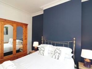 Un dormitorio con un espejo grande, estructura metálica para la cama, ropa de cama blanca y dos lámparas de noche.