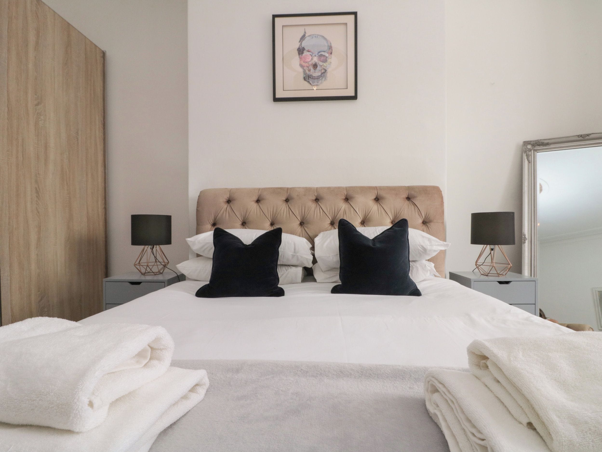 Una habitación de hotel con una cama grande, dos mesitas de noche con lámparas, un cuadro enmarcado en la pared y un armario.