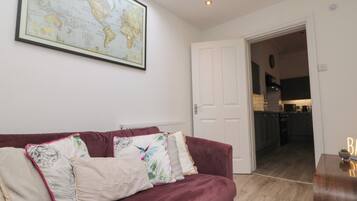 A living room with a large world map on the wall, a red sofa with decorative pillows, and a view into the kitchen.