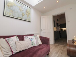 A living room with a large world map on the wall, a red sofa with decorative pillows, and a view into the kitchen. - Royal Victoria House (Scarborough)