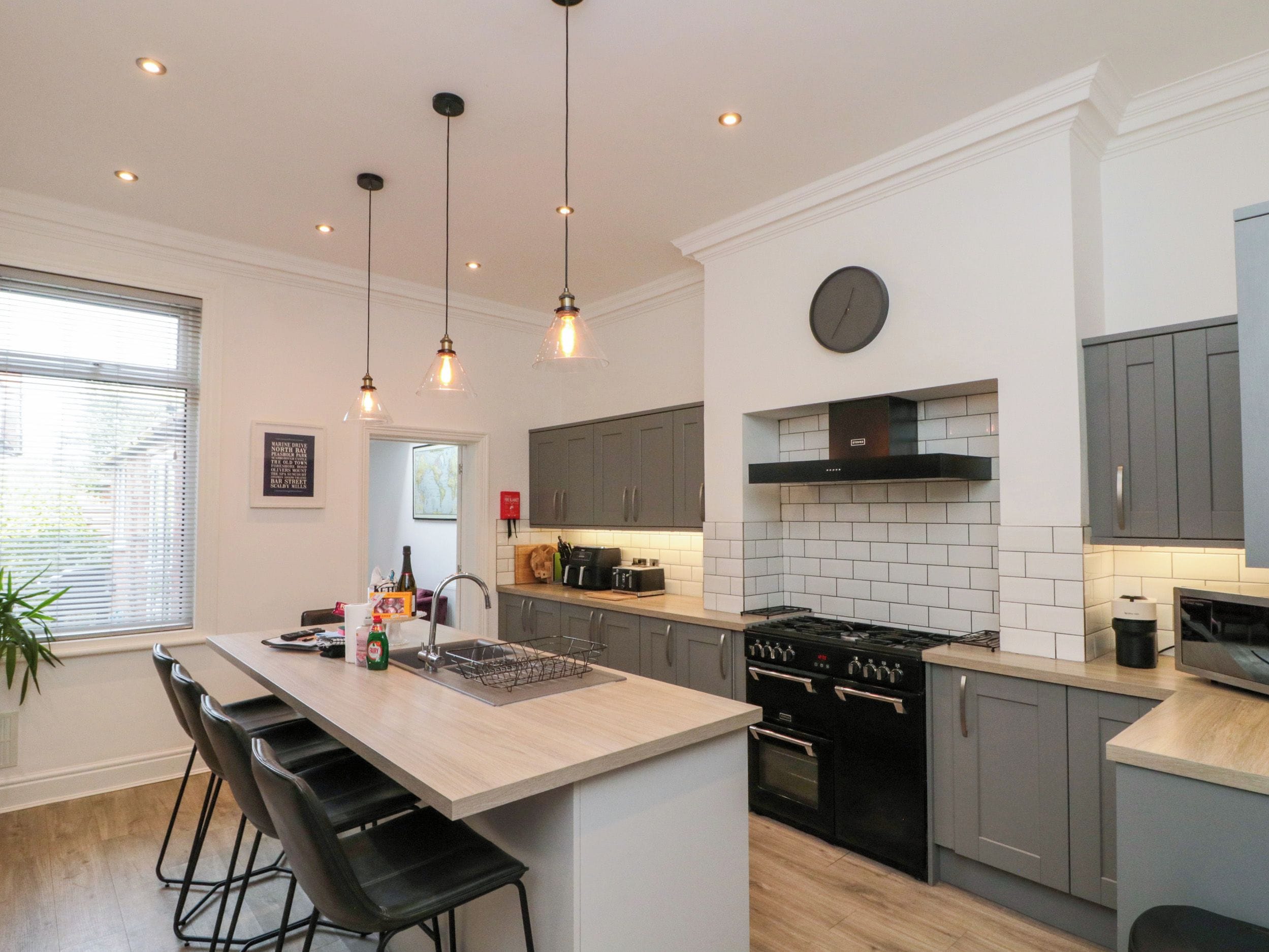 Una cocina moderna con una isla central, iluminación colgante y un reloj en la pared.