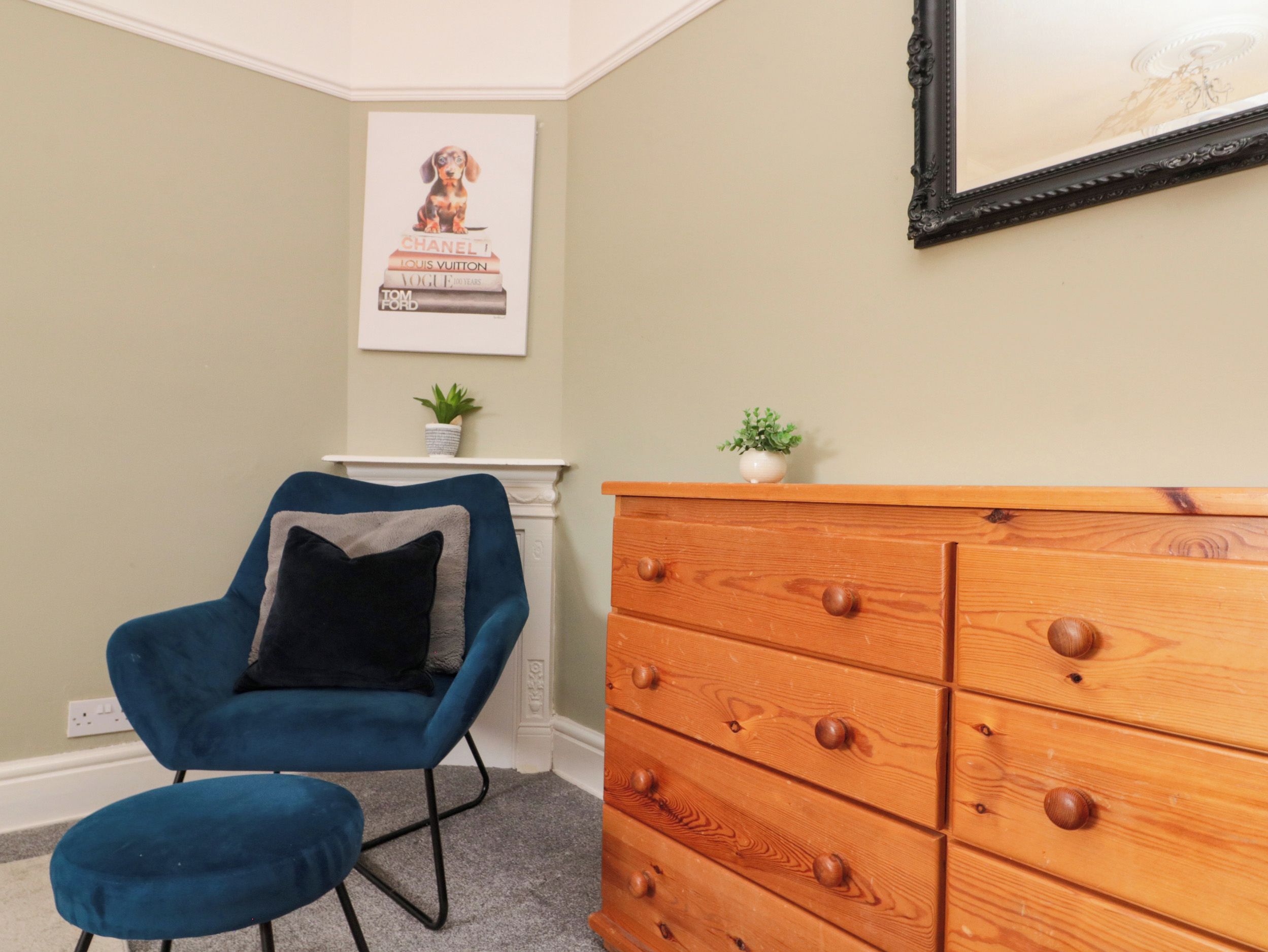 A room with a blue armchair, a wooden dresser, and a framed poster on the wall.